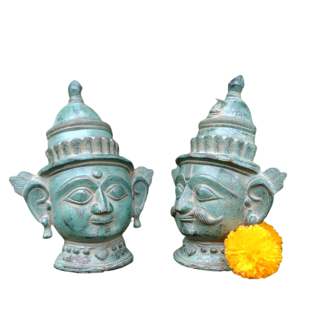 Two decorative urns with face designs on a stone surface with greenery in the background